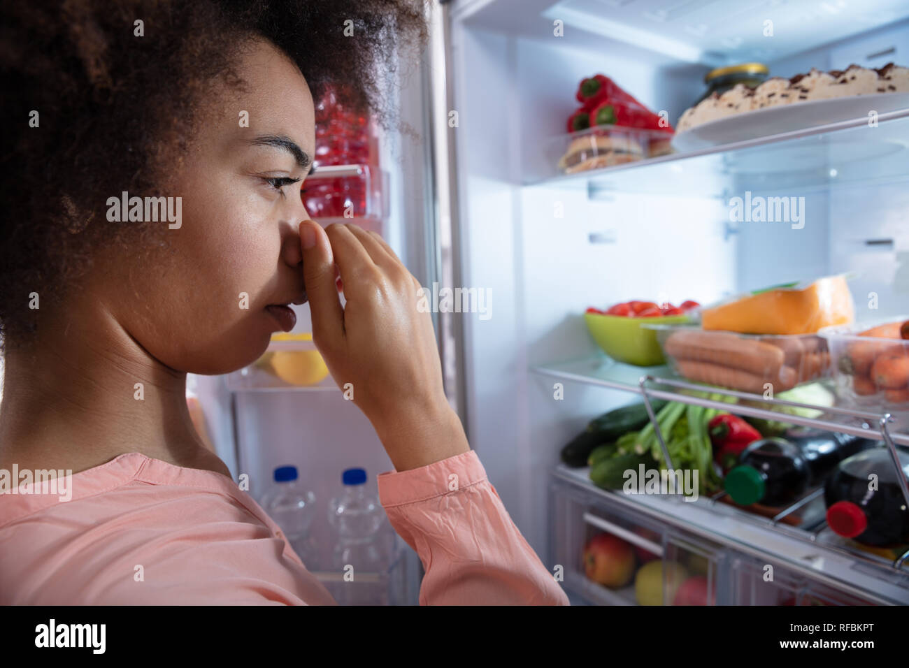Vue latérale du jeune femme reconnaissant Mauvaise odeur provenant du réfrigérateur, couvrant son nez Banque D'Images