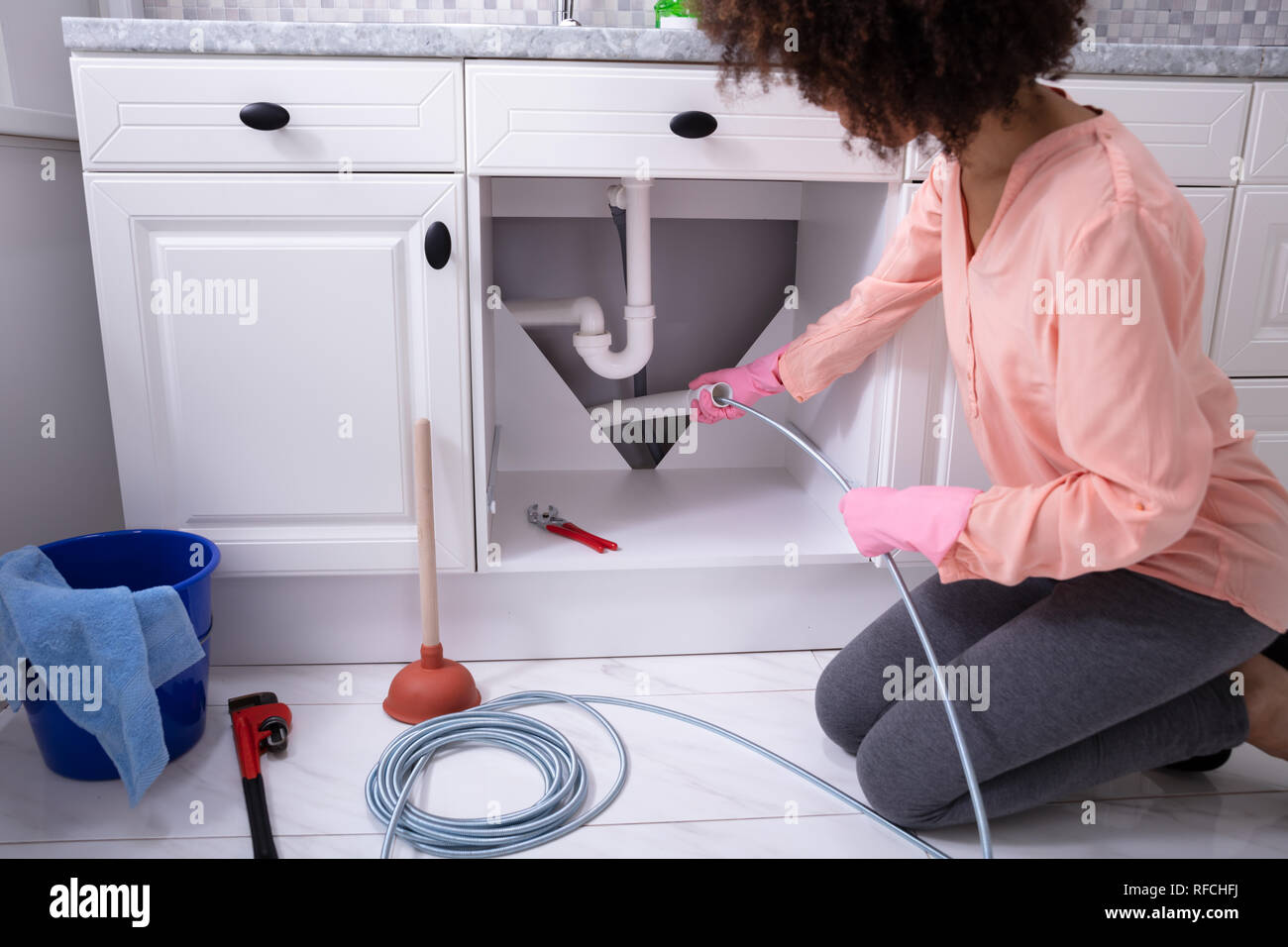 Une jeune femme en train de nettoyer le tuyau de l'évier bouché avec câble  drainés dans la cuisine Photo Stock - Alamy