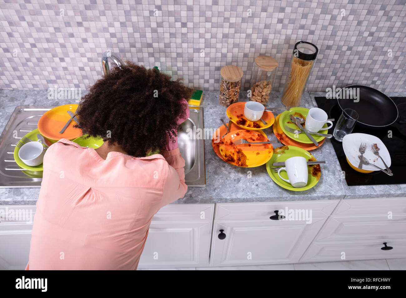 Assez jeune femme se penchant près de l'évier avec des ustensiles colorés sales dans la cuisine Banque D'Images