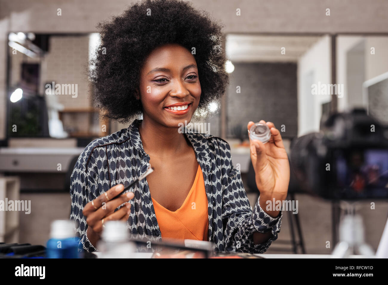 Sourire femme à la peau sombre avec des cheveux bouclés démontrant une nouvelle ombre à paupière swatch Banque D'Images