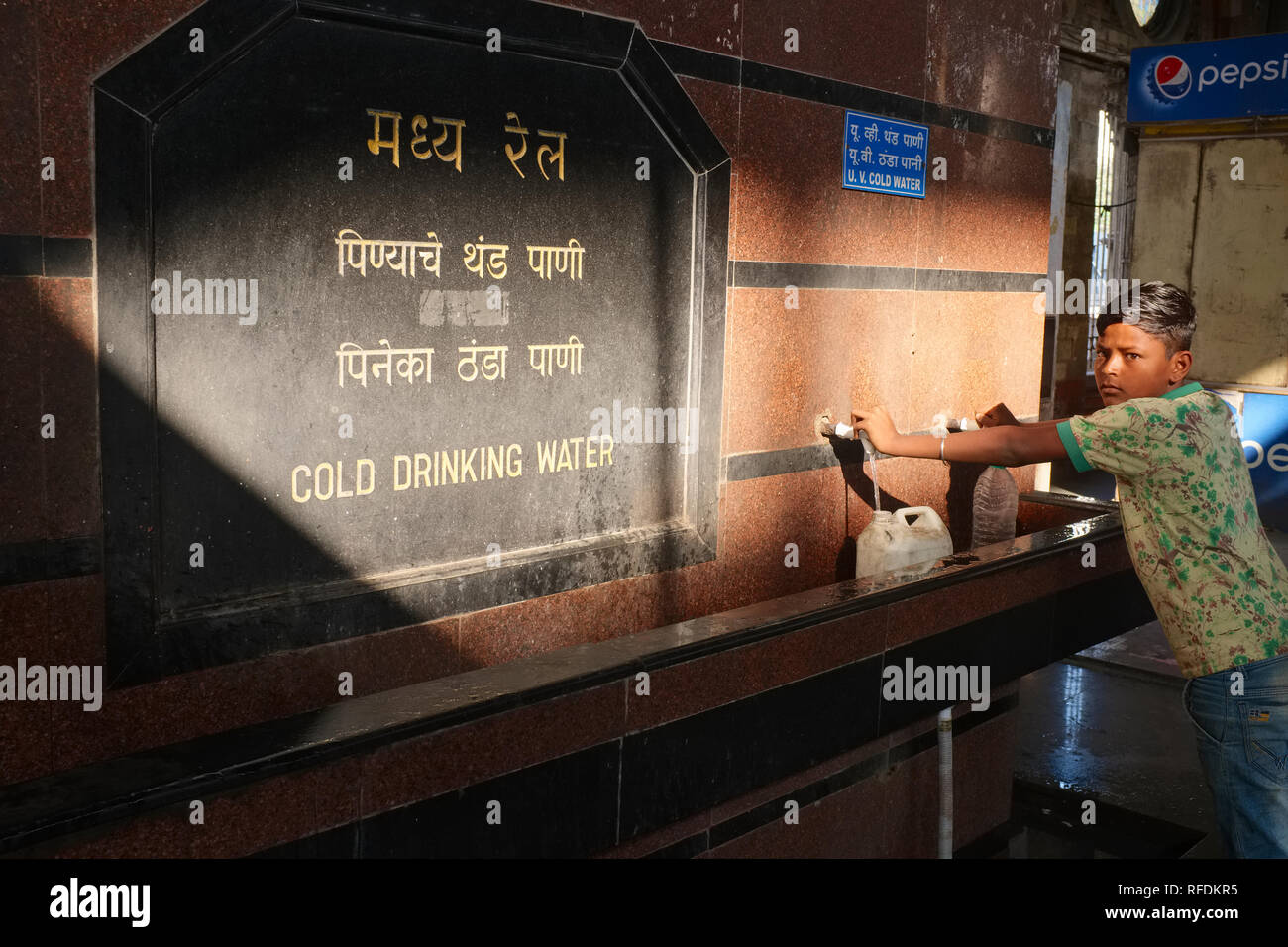 Un garçon à Maharaj Chhatrapati Shivaji Terminus (CSMT) à Mumbai, Inde, prend de l'eau d'une fontaine d'eau public Banque D'Images