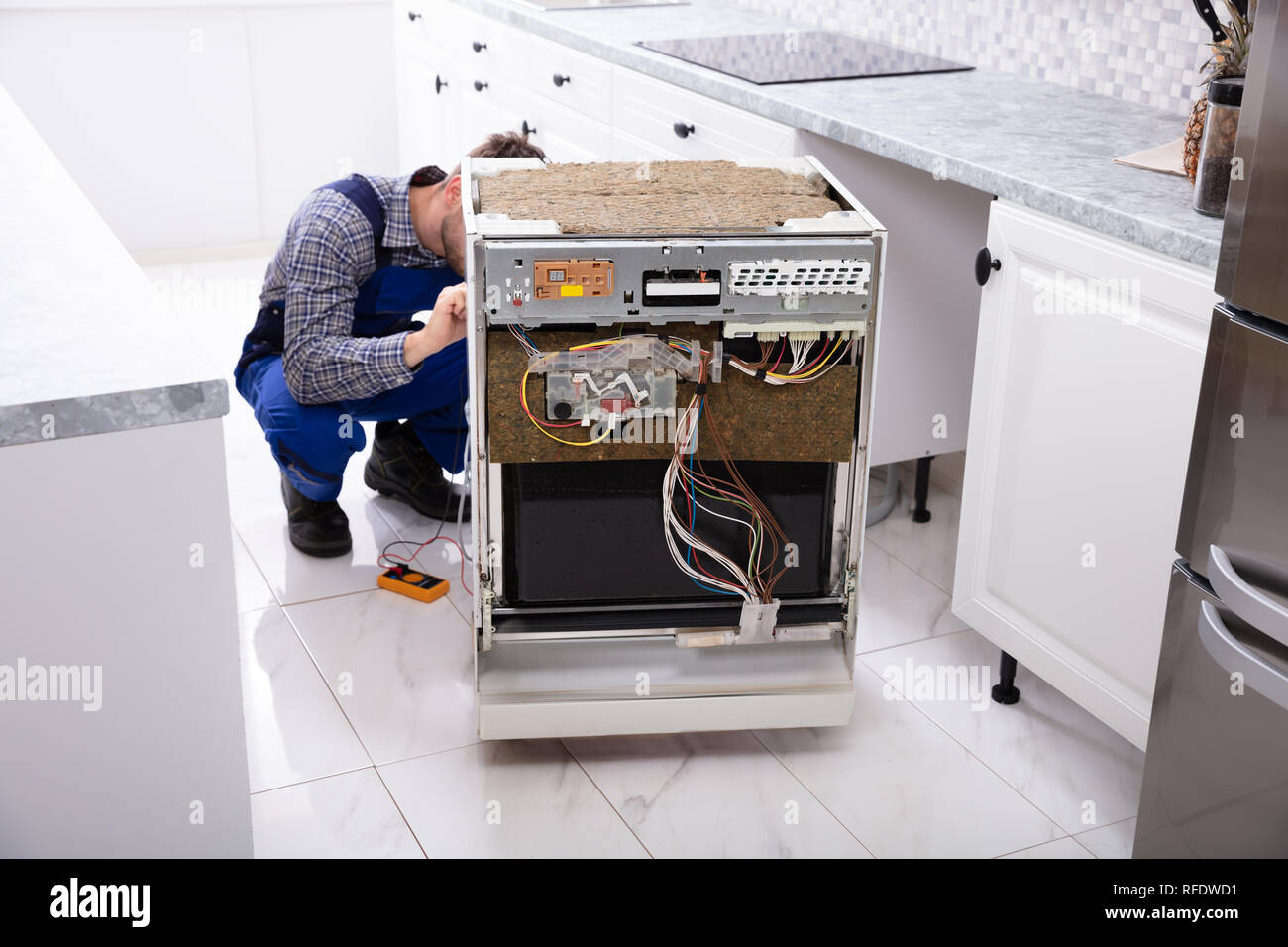 Jeune réparateur lave-vaisselle Fixation avec multimètre numérique en cuisine Banque D'Images