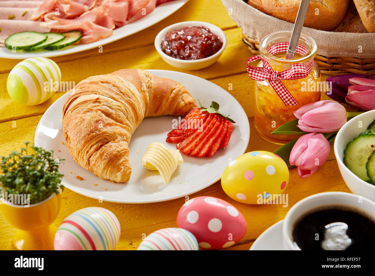 Délicieux petit-déjeuner de Pâques sur une table décorée avec des oeufs colorés et un croissant et du four avec la confiture de fraise, de la charcuterie, du fromage un Banque D'Images