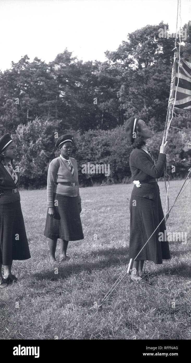 Années 1950, historiques, trois British Girl Guides en uniforme à l'extérieur dans un champ de mettre en place un drapeau Union-Jack à leur camping, England, UK. La fille des GUID ont été officiellement créé en 1910 deux ans après la création du mouvement scout. Banque D'Images