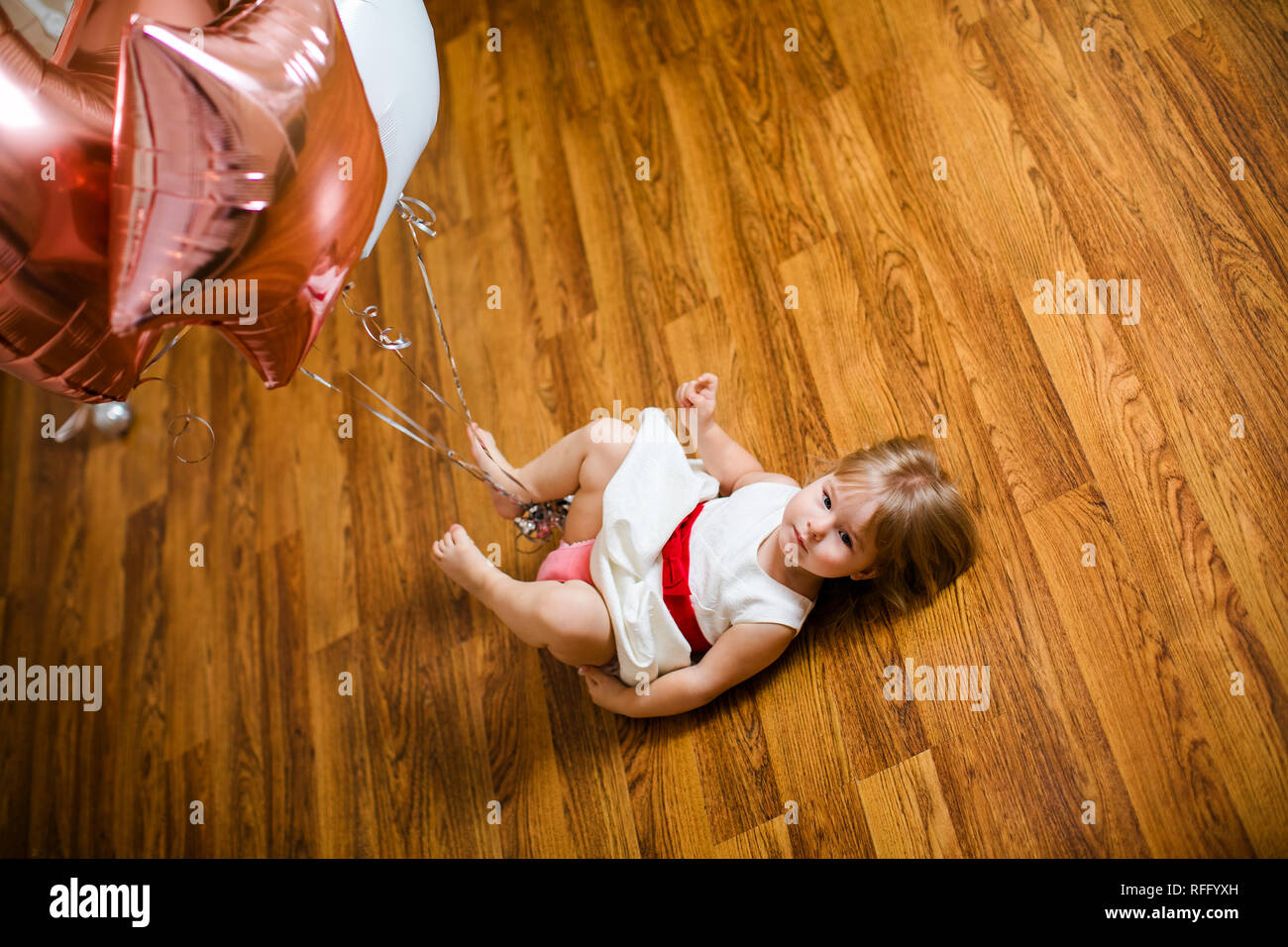 Petite blonde fille bébé deux ans avec de grands ballons rose et blanc couché sur le plancher en bois sur son anniversaire. Banque D'Images