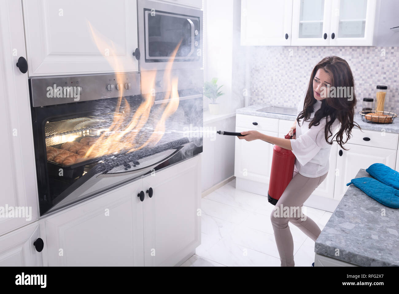 Femme à l'aide d'extincteur pour feu stop en sortant du four dans la cuisine Banque D'Images