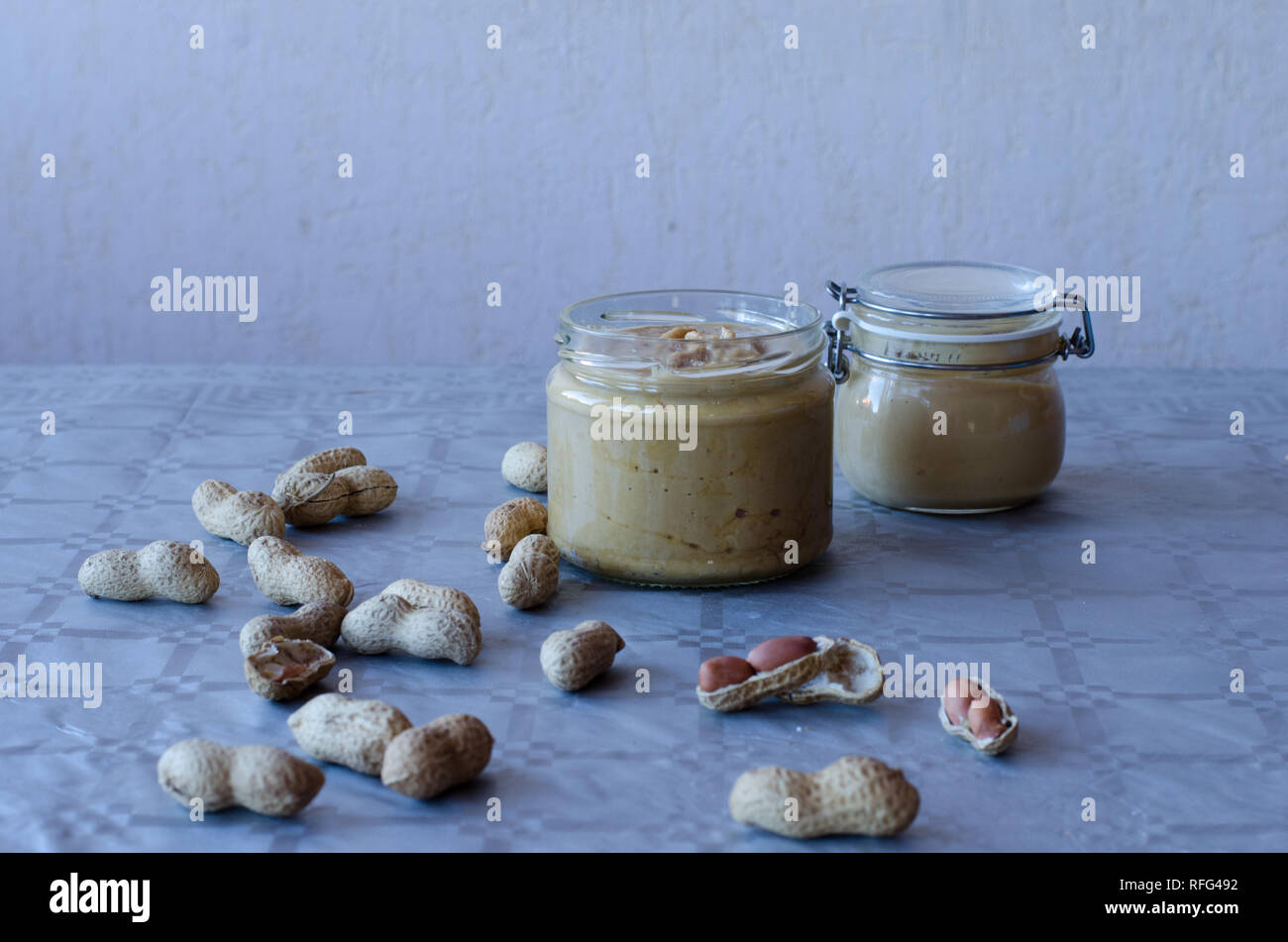 Beurre de cacahuète fait maison dans un bocal en verre avec des cacahuètes réparties sur la table Banque D'Images Beurre de cacahuète fait maison dans un bocal en verre avec des cacahuètes réparties sur la table Banque D'Images