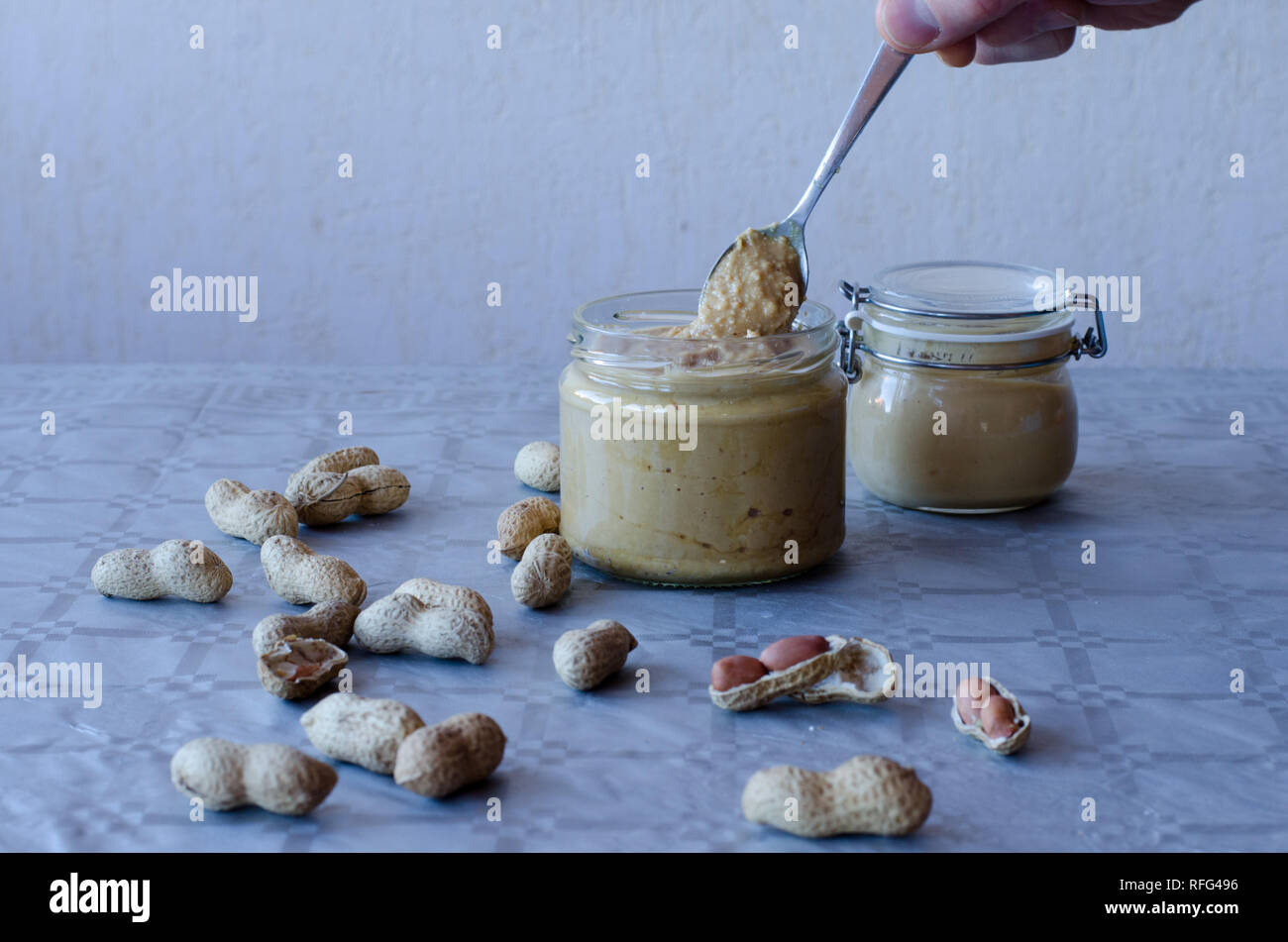 Beurre de cacahuète fait maison dans un bocal en verre avec des cacahuètes réparties sur la table Banque D'Images Beurre de cacahuète fait maison dans un bocal en verre avec des cacahuètes réparties sur la table Banque D'Images