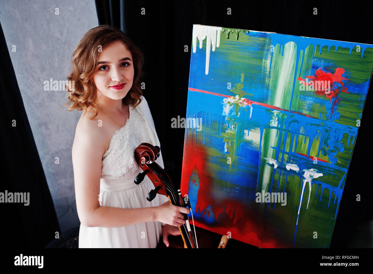 Jeune musicien gilrl en robe blanche avec la contrebasse à côté de son art de peindre. Banque D'Images