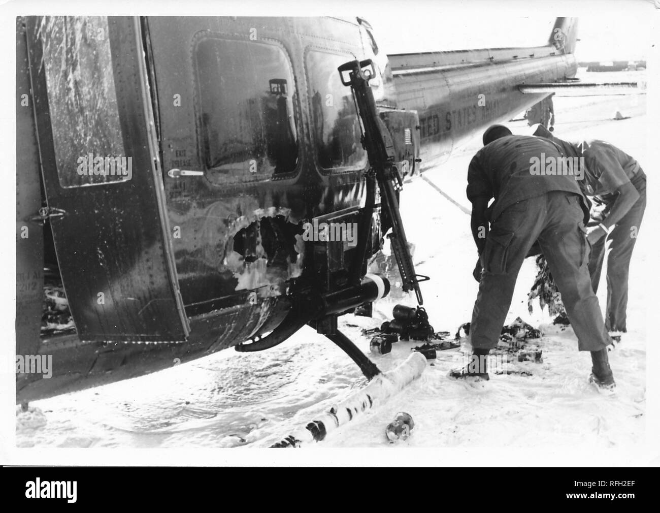 Photographie noir et blanc, montrant deux hommes en uniformes militaires, se penchant pour l'enquête de dommage subi par un Bell UH-1 Huey' ('Iroquois) hélicoptère, avec une substance de couleur claire (peut-être le sable, la neige ou mousse) visible sur le terrain, photographié lors de la guerre du Vietnam, 1968. () Banque D'Images