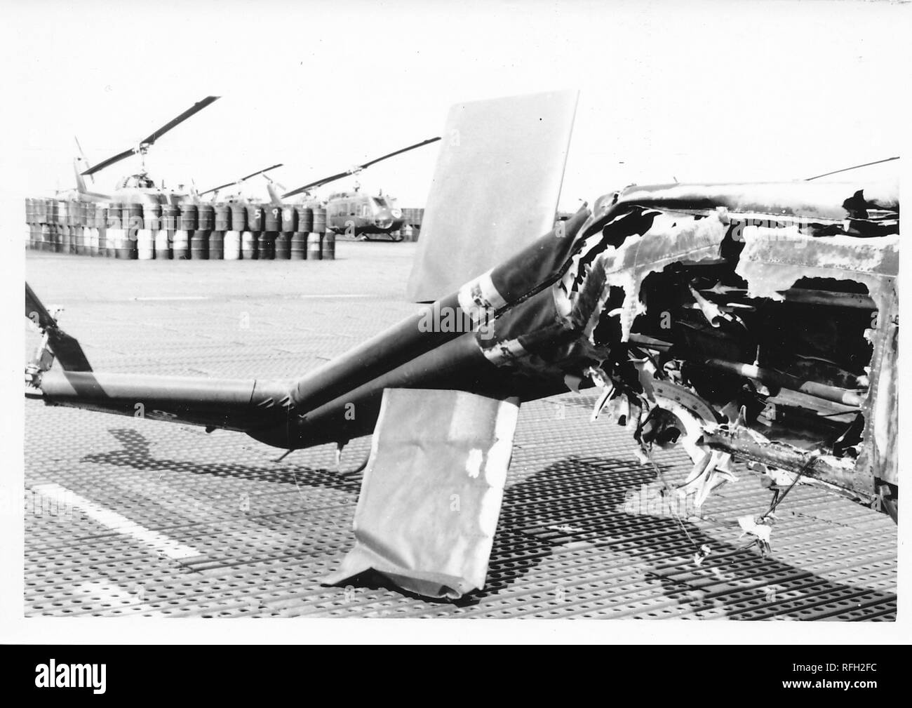 Photographie noir et blanc, montrant l'endommagea de queue et la section de montage du moteur d'un hélicoptère militaire, probablement un Bell UH-1 Huey Iroquois ('') avec barils et plus d'hélicoptères visible à l'arrière-plan, photographié lors de la guerre du Vietnam, 1968. () Banque D'Images
