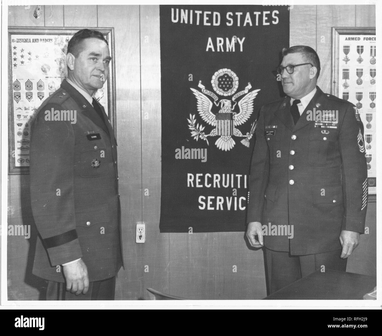 Photographie en noir et blanc de deux hommes d'âge moyen, chaque comité permanent en vue trois-quarts, portant des uniformes militaires US, avec le général de brigade Frank L Gunn (à gauche) montre le profil de partielle, avec une atmosphère d'expression sur son visage, l'homme à droite porte des lunettes et visages Gunn général, des affiches avec des images des insignes, écussons, et des médailles, et un signe avec le texte 'United States Army Recrutement Services, ' sont visibles en arrière-plan, photographié lors de la guerre du Vietnam, 1967. () Banque D'Images