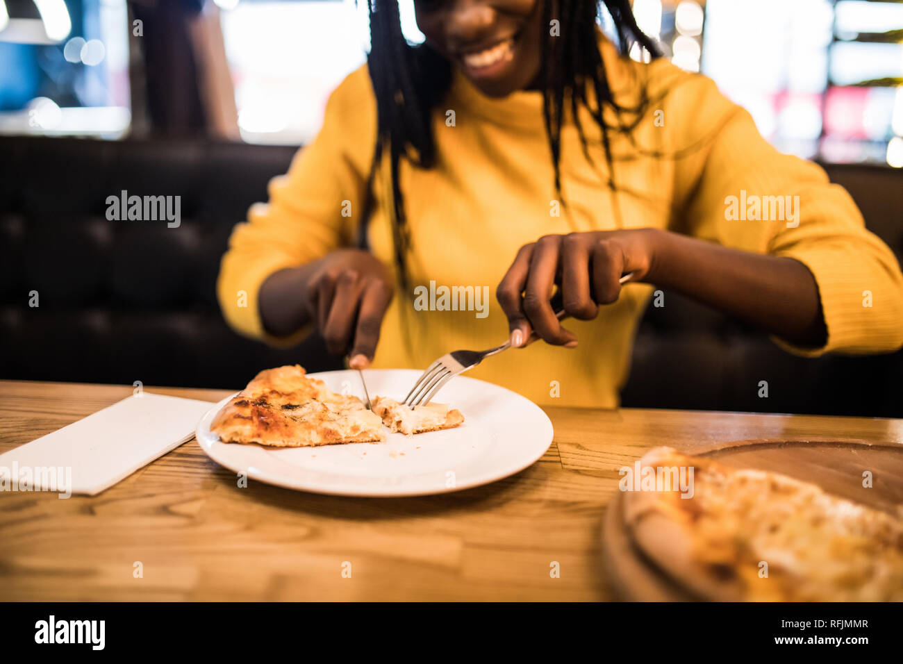 Les jeunes afro american woman wearing dans chandail jaune eating pizza in cafe Banque D'Images