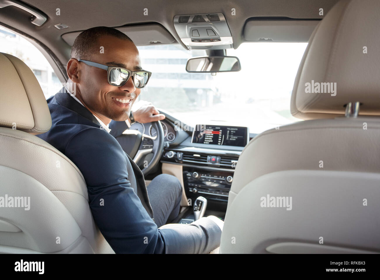 Jeune homme à lunettes pilote assis à l'intérieur à la voiture à l'arrière siège arrière de l'appareil photo sur joyeuse Banque D'Images