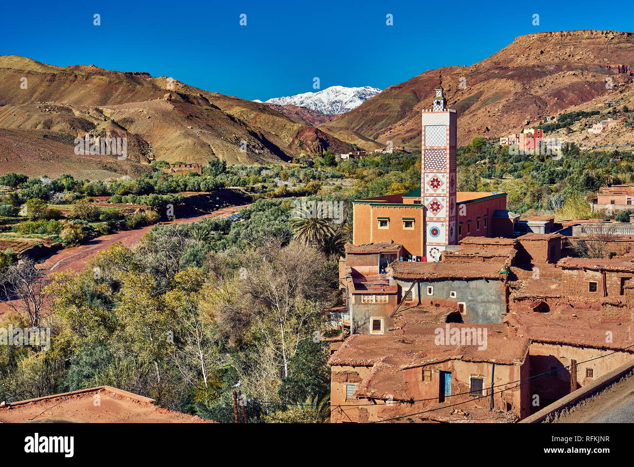 Maisons de village en briques de boue traditionnelles, minaret/mosquée à la décoration colorée avec montagnes enneigées de l'Atlas. Pris près de Tiseldei, Ouarzazate, Maroc Banque D'Images