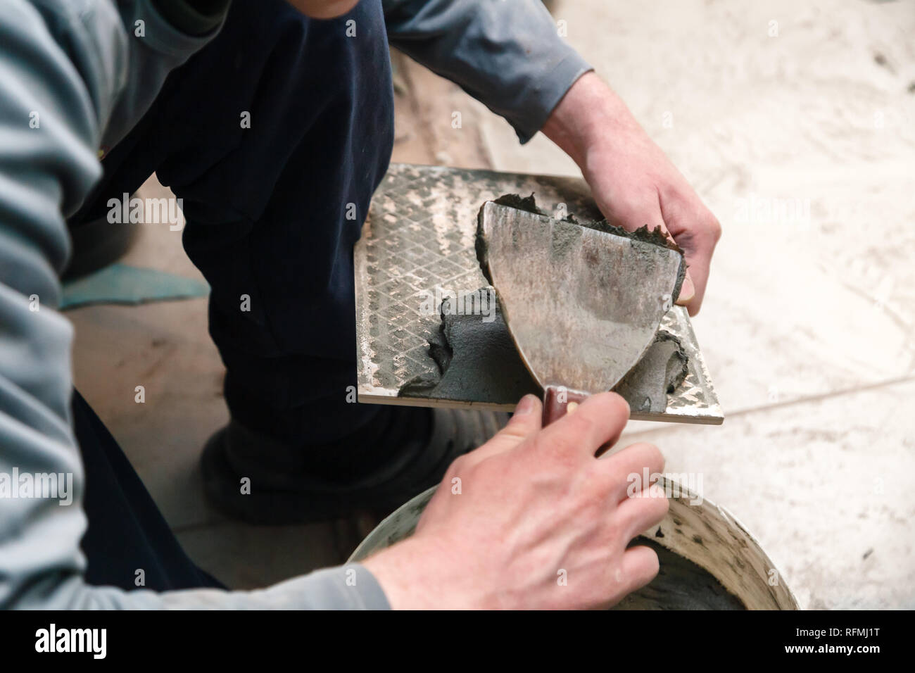 La main libre de constructeur ciment colle sur le frottis en carreaux de céramique avec une truelle pour colle dans la salle de bains privative. Concept Rénovation Réparation, révision, contrat carreleur Banque D'Images