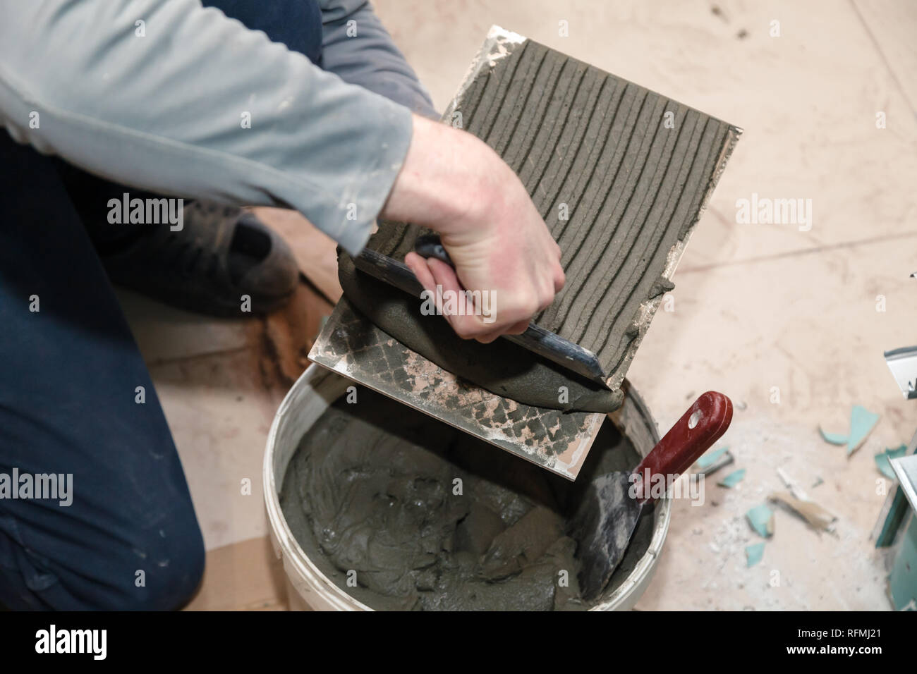 La main libre de constructeur ciment colle sur le frottis en carreaux de céramique avec une truelle pour colle dans la salle de bains privative. Concept Rénovation Réparation, révision, contrat carreleur Banque D'Images