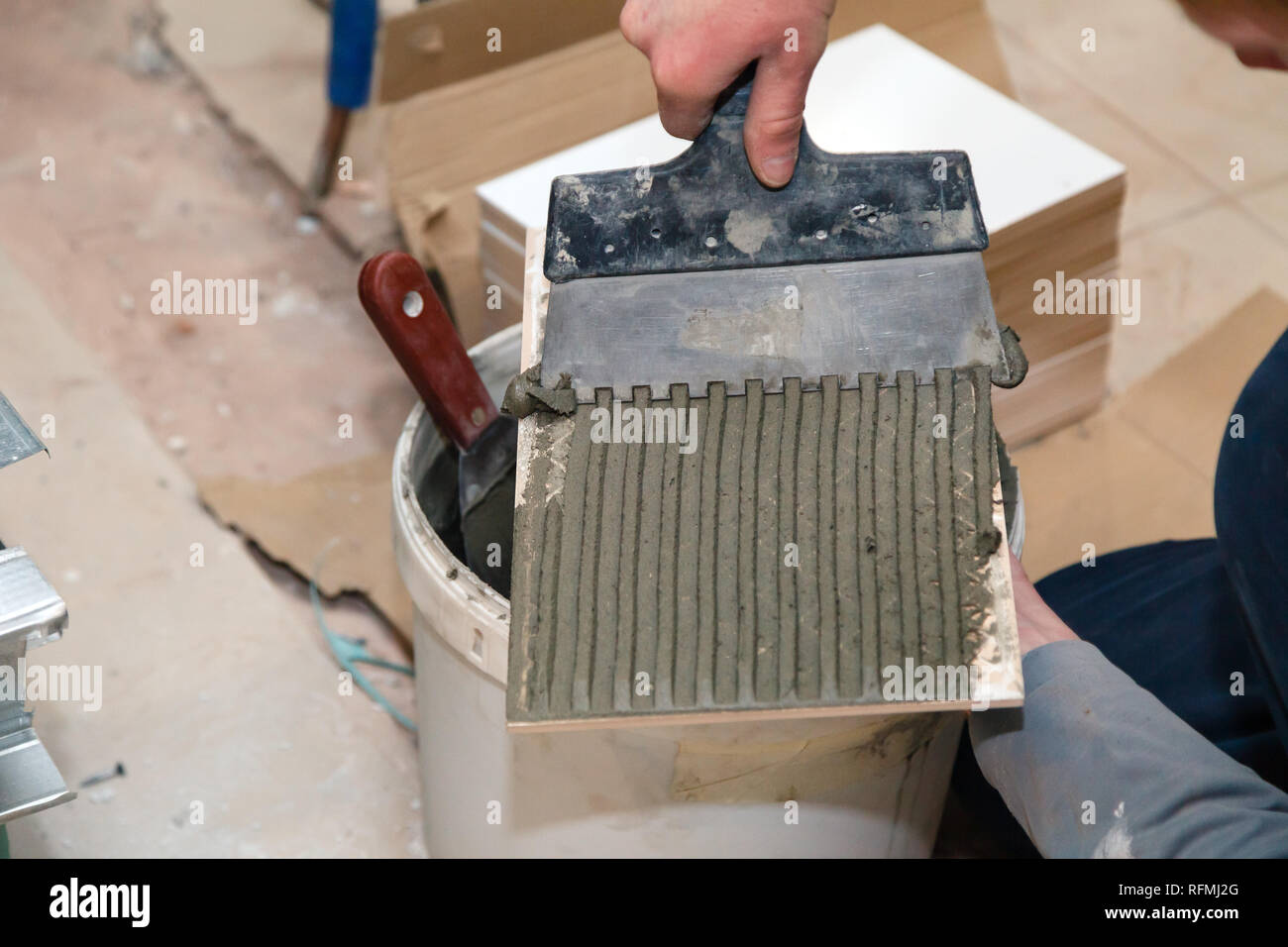 La main libre de constructeur ciment colle sur le frottis en carreaux de céramique avec une truelle pour colle dans la salle de bains privative. Concept Rénovation Réparation, révision, contrat carreleur Banque D'Images