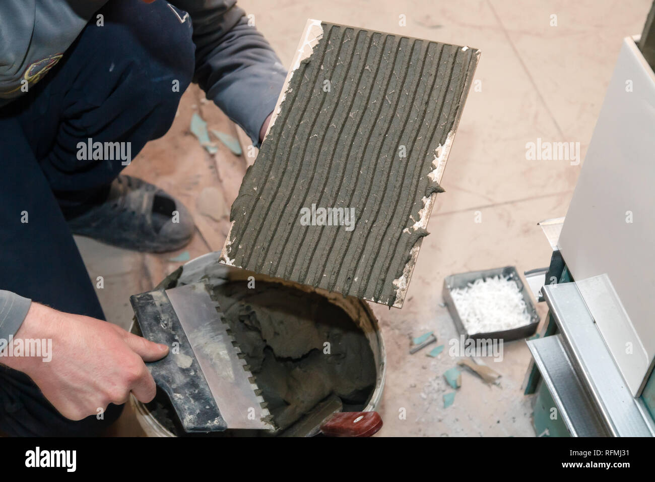 La main libre de constructeur ciment colle sur le frottis en carreaux de céramique avec une truelle pour colle dans la salle de bains privative. Concept Rénovation Réparation, révision, contrat carreleur Banque D'Images