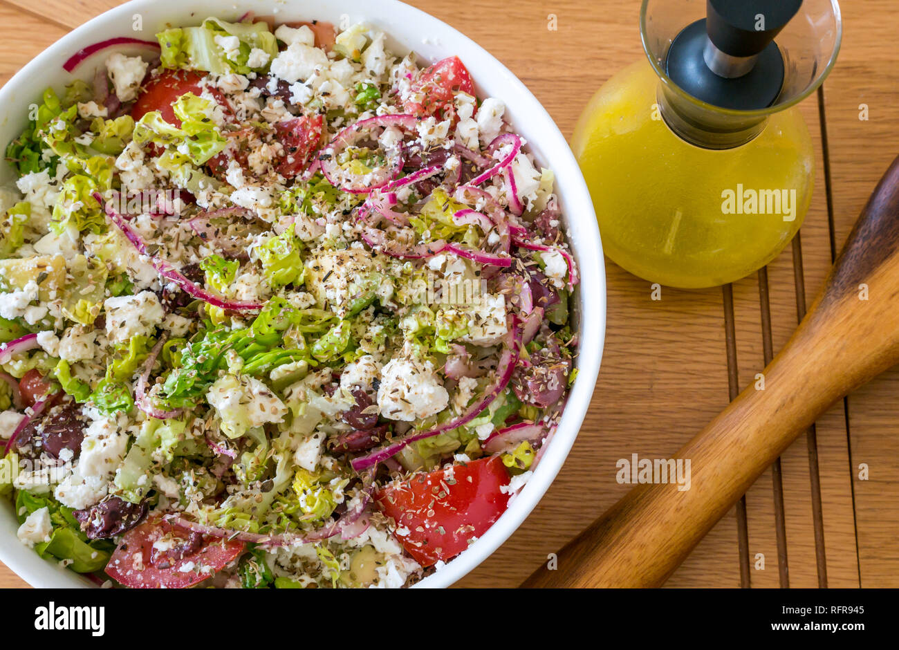 Vaisselle blanche saladier rempli de salade grecque avec fromage feta, tomates, oignons rouges, avocat, laitue et vinaigrette de citron dans un bocal en verre Banque D'Images