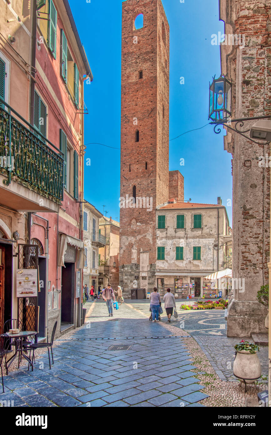 Ancienne tour médiévale dans un carré à Noli, Ligurie, Italie avec des piétons font leur shopping sur une allée pavée in early morning light Banque D'Images
