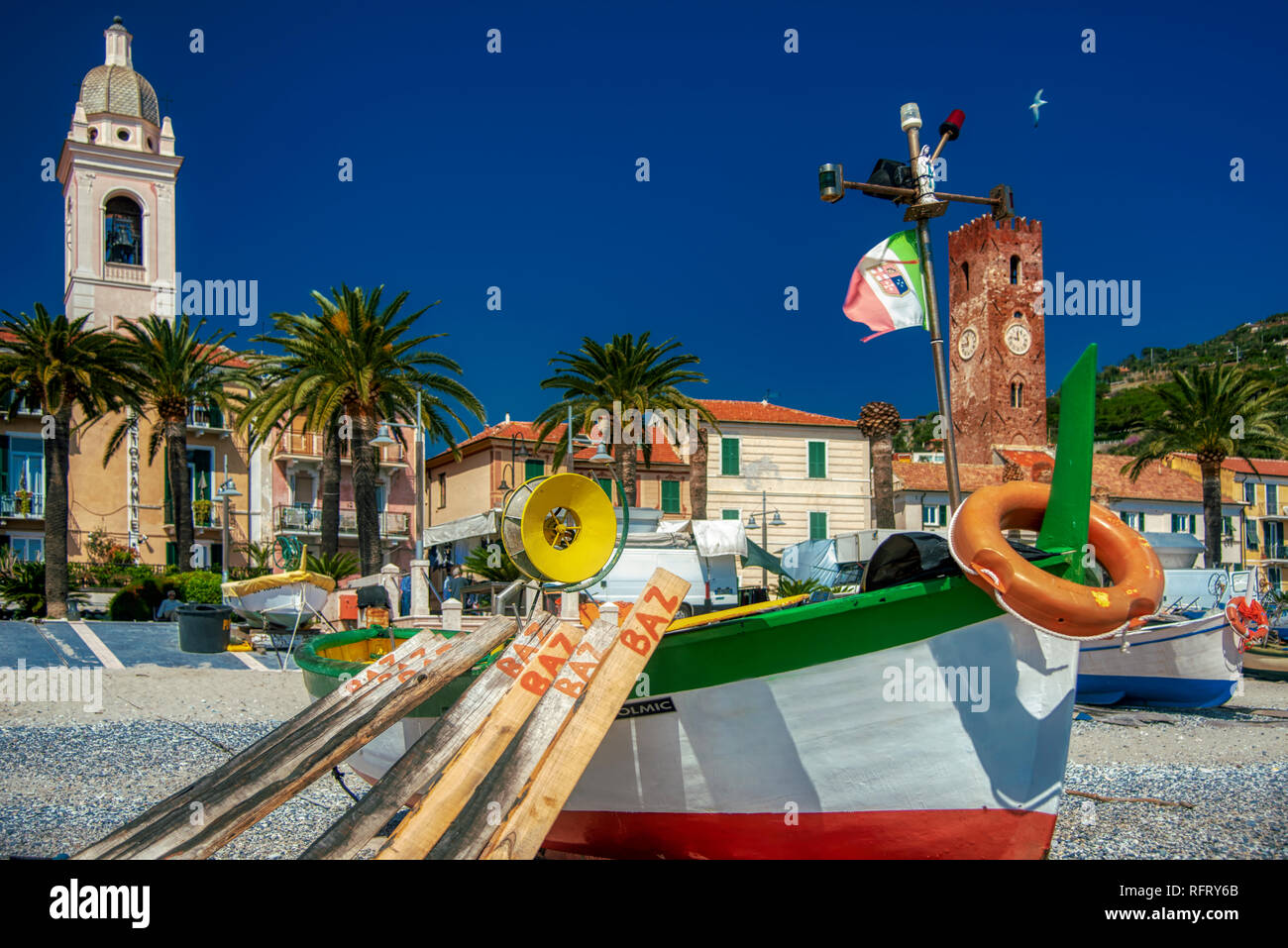 Vieux bateaux de pêche en bois colorés sur la plage, Noli, l'Italie médiévale historique avec des bâtiments au bord de l'eau derrière et de palmiers tropicaux sur la promenad Banque D'Images
