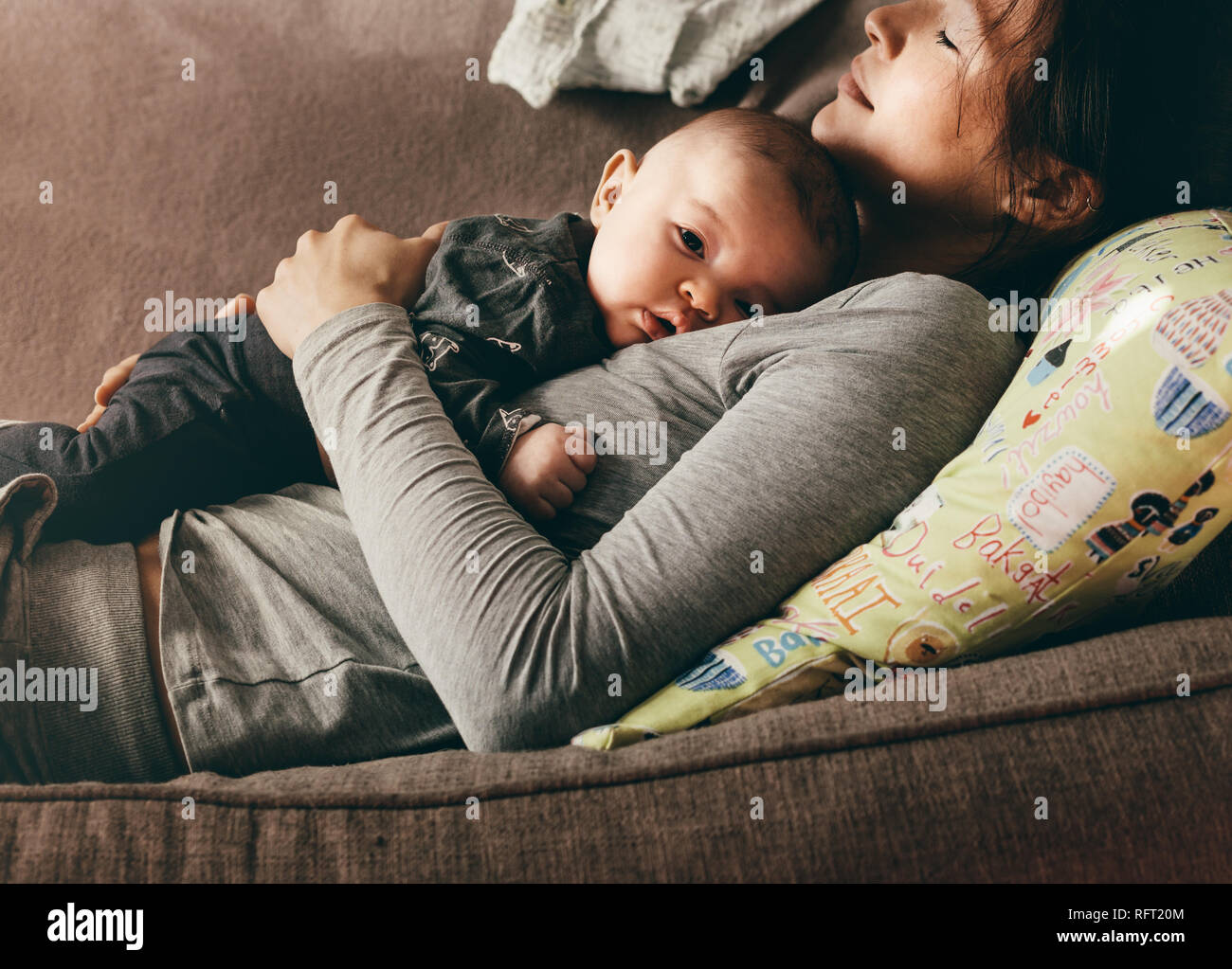 Mère qui reste dormir sur un canapé avec son bébé sur sa poitrine. Gros plan d'une femme couchée sur un canapé avec son bébé posé sur elle. Banque D'Images