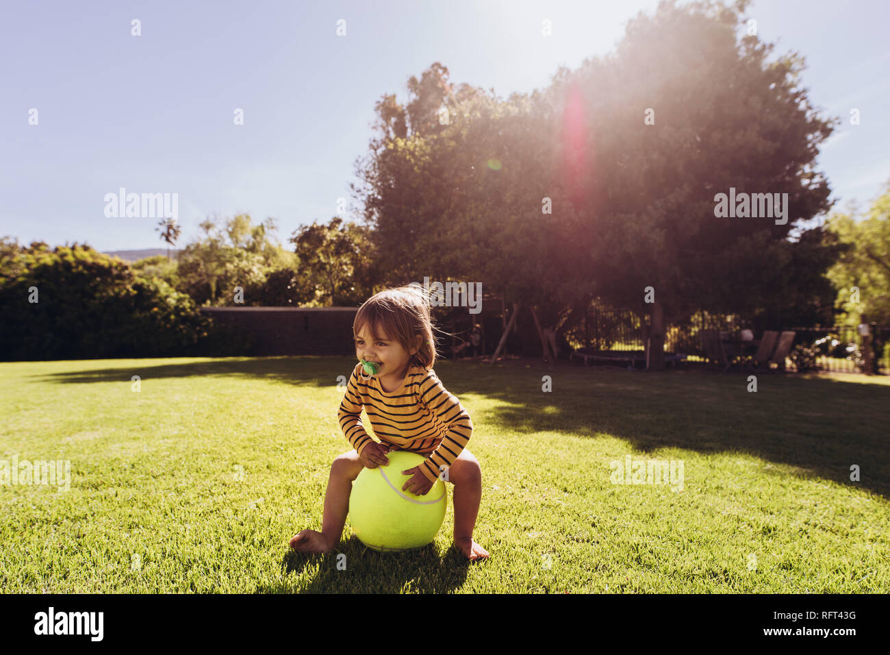 Little boy playing with ball dans un parc sur une journée ensoleillée. Smiling boy jouer seul dans le parc avec sun flare en arrière-plan. Banque D'Images