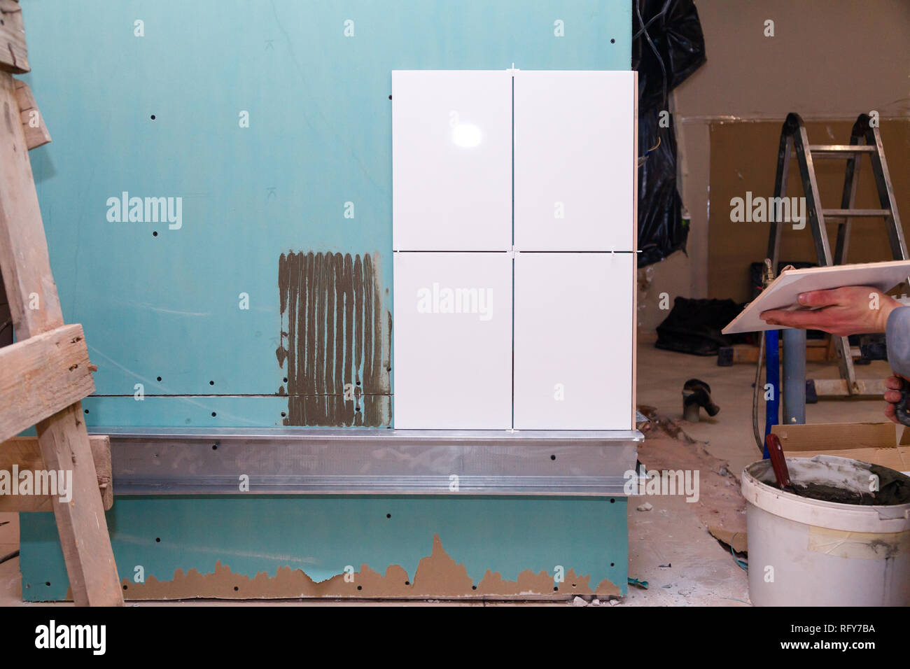 Réparation de gros plan, carreaux de céramique blanche avec de l'adhésif sur les panneaux de plâtre dans la salle de bains, constructeur professionnel de la main de l'homme. Concept Rénovation Réparation, révision, contrac Banque D'Images