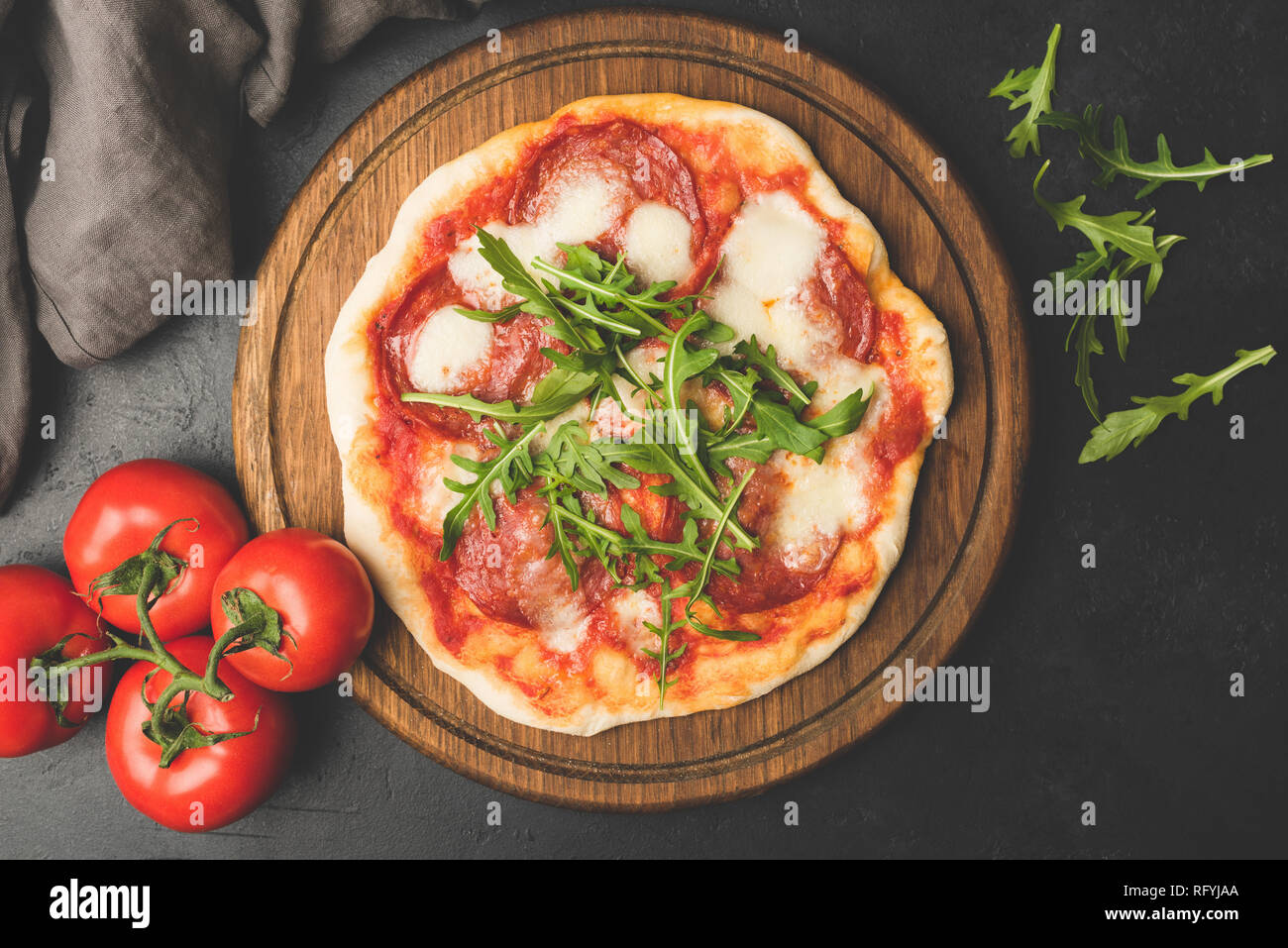 Pizza savoureuse avec tomate Mozzarella Salami sur planche de bois. Pizza garnie de feuilles de roquette. La cuisine Italienne Banque D'Images