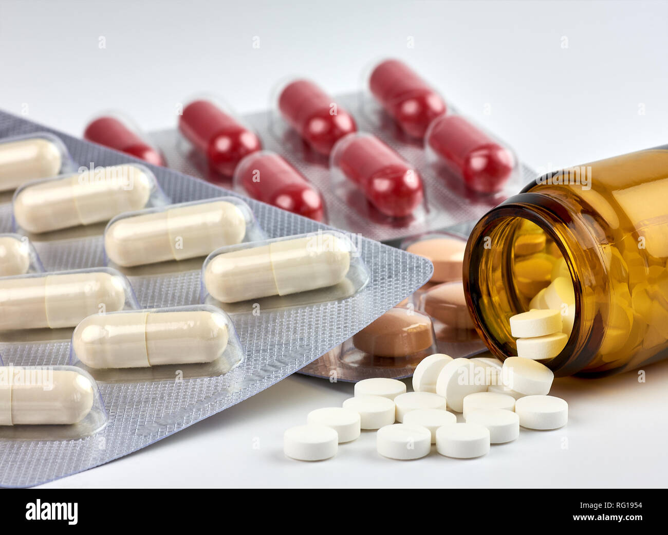 Vue rapprochée de pilules colorées et drogues déversés par un médicament sur une bouteille brune floue fond blanc Banque D'Images