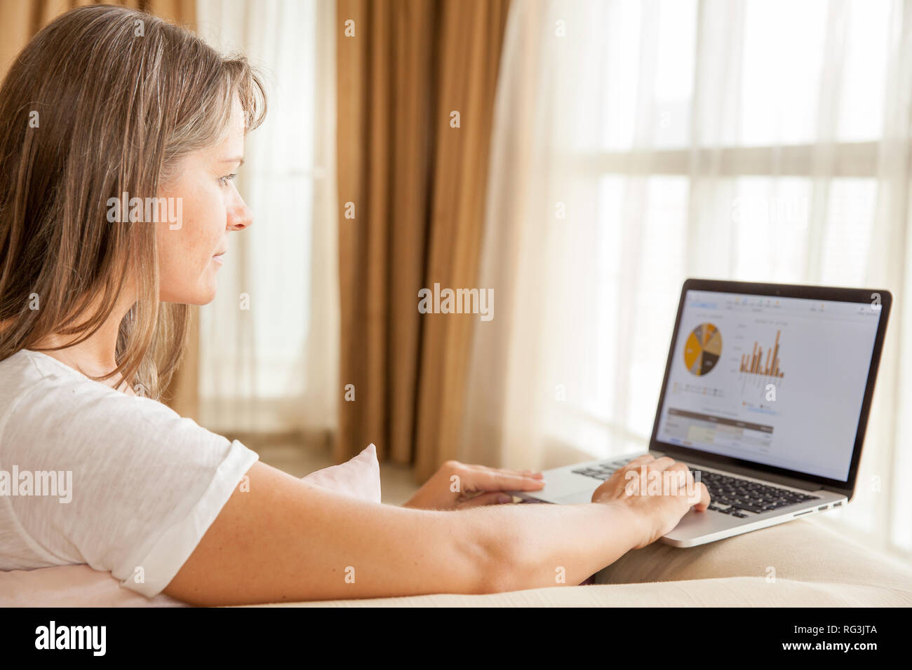 Jolie femme mature travaille sur un ordinateur portable tout en étant assis sur un canapé dans sa salle de séjour Banque D'Images