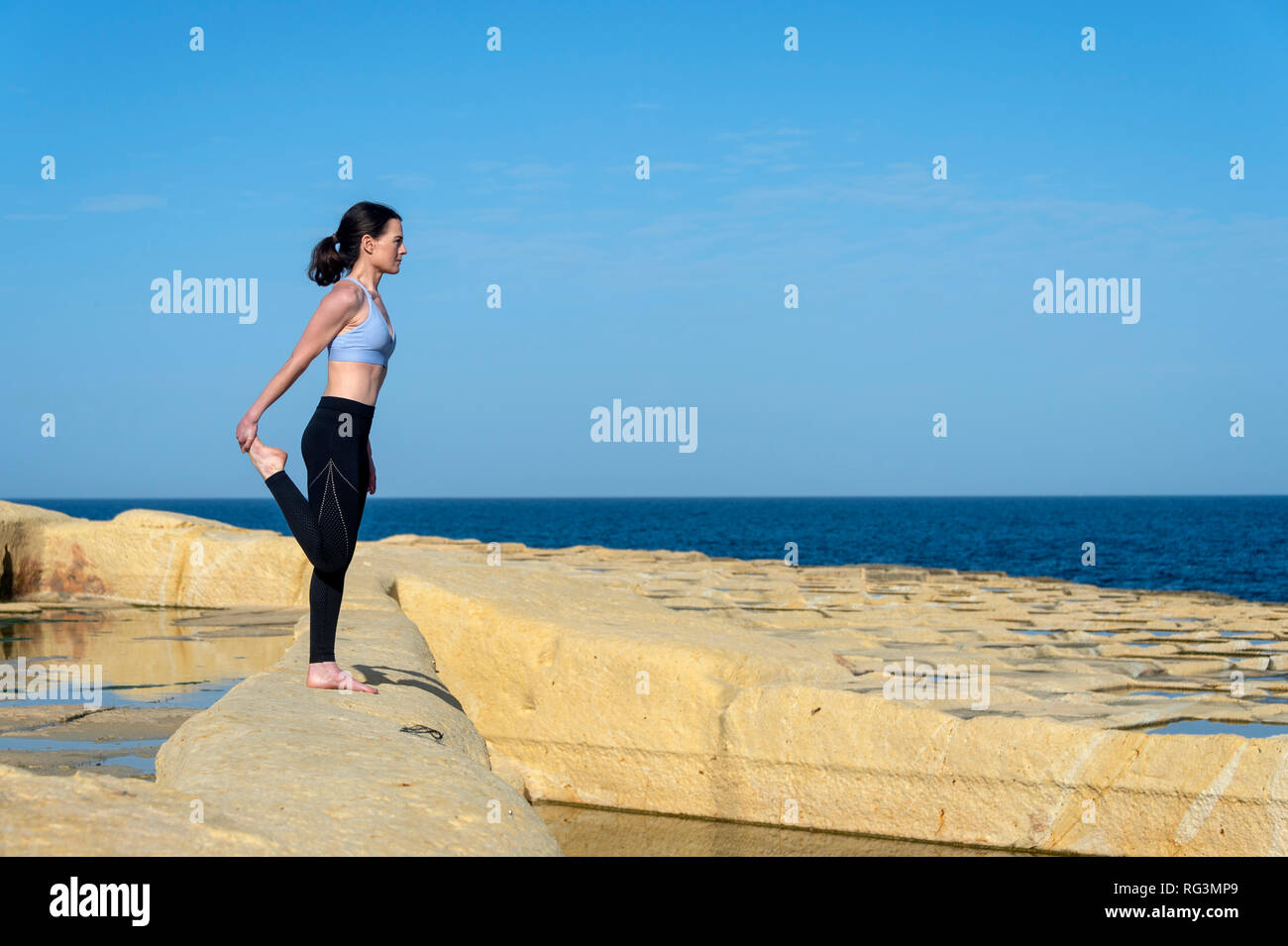 Vue latérale d'une femme faisant un quad stretch à l'extérieur par la mer le port d'un soutien-gorge de sport et leggings Banque D'Images
