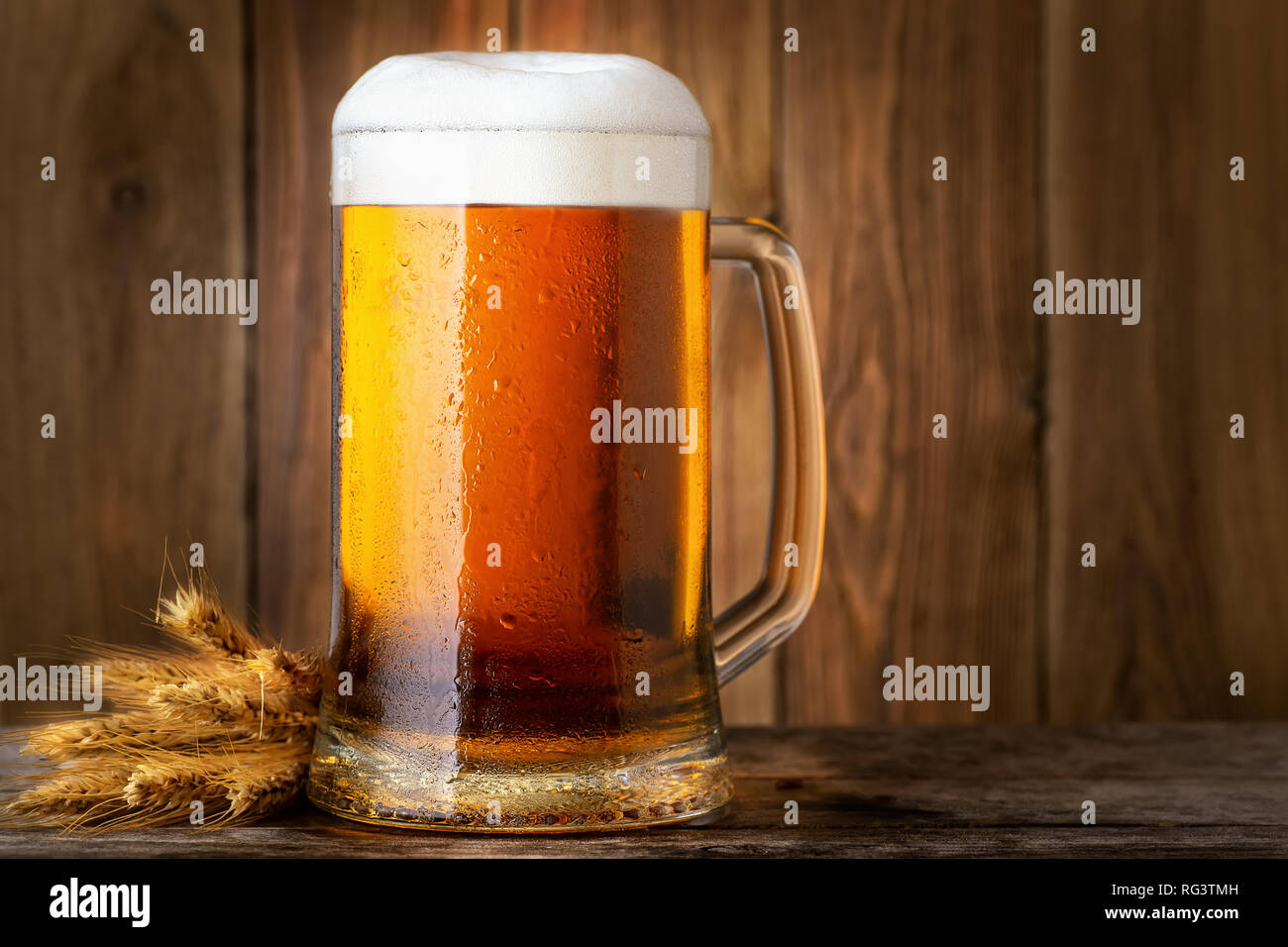 Chope de bière légère froide avec les épis de blé sur table en bois Banque D'Images