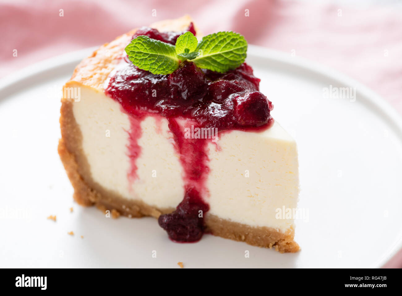 Gâteau au fromage avec coulis de cerise sucrée sur une assiette décorée avec des feuilles de menthe. Vue rapprochée. Tranche de gâteau savoureux Banque D'Images