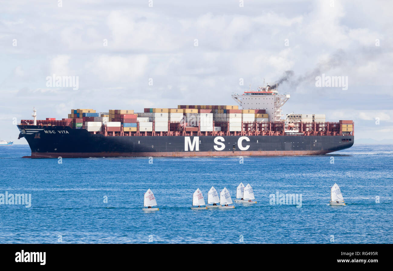 Fumée noire émettant des conteneurs passant de petits bateaux à voile lorsqu'il entre dans le port. Banque D'Images