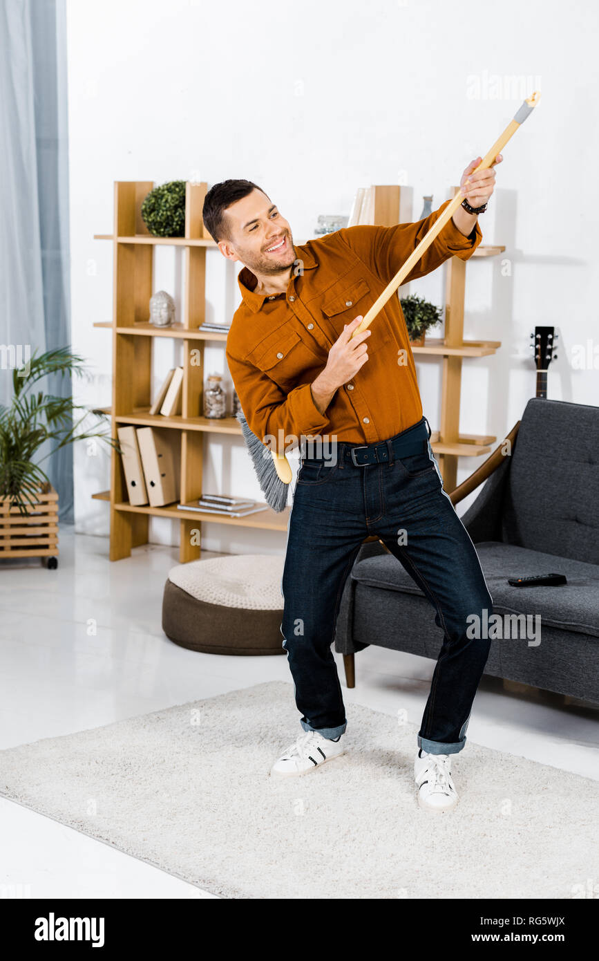 Handsome man dancing with broom in modern living room Banque D'Images