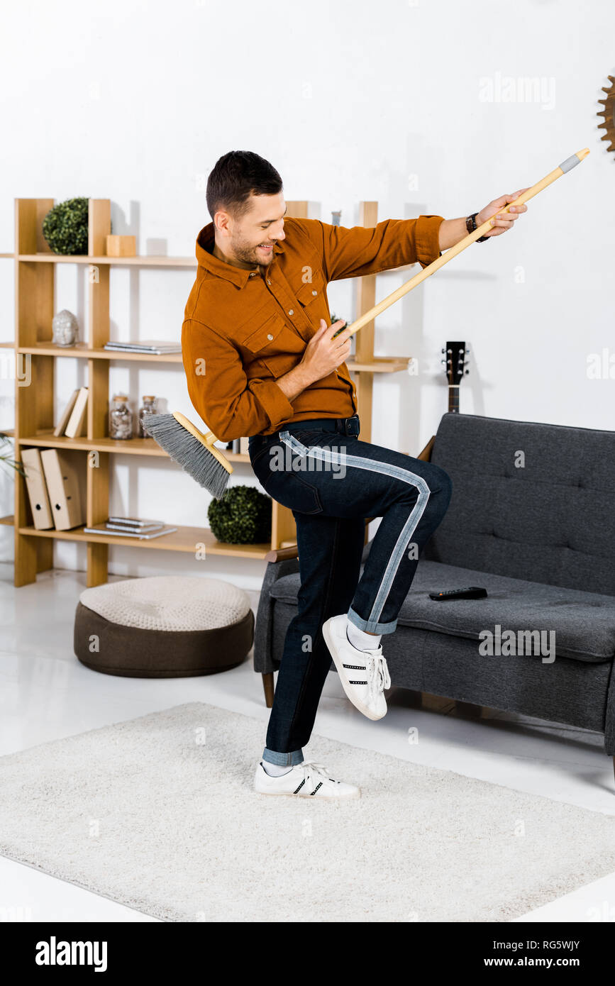 Cheerful man dancing with broom in modern living room Banque D'Images
