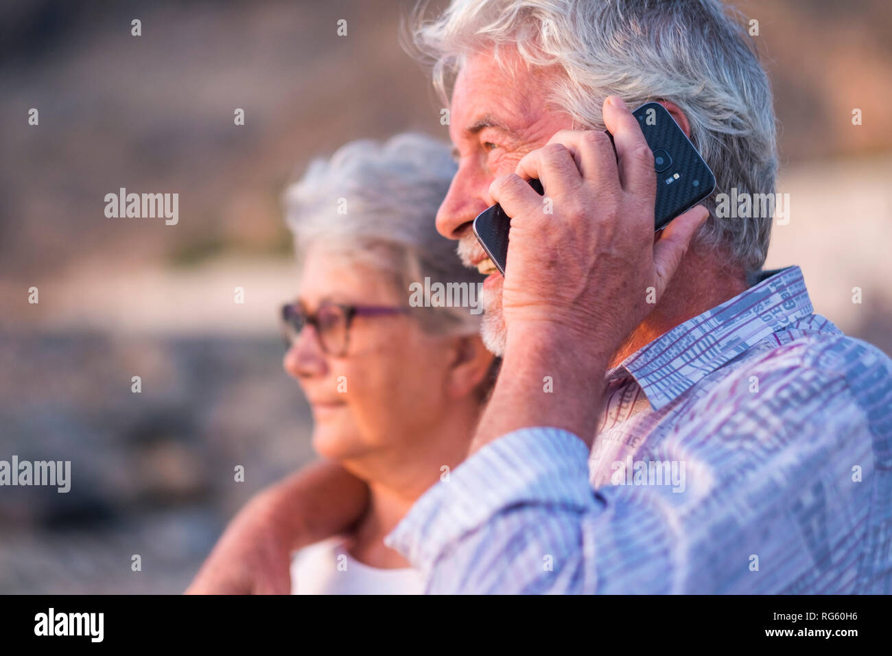 Heureux couple retraité de man et femme gens hug et regarder en face d'eux en utilisant et en parlant avec la technologie moderne smart phone - moderne li Banque D'Images