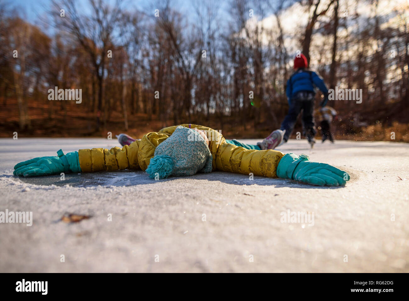 Fille couchée sur un étang gelé avec ses bras tendus et deux personnes, le patin à glace à l'arrière-plan, United States Banque D'Images