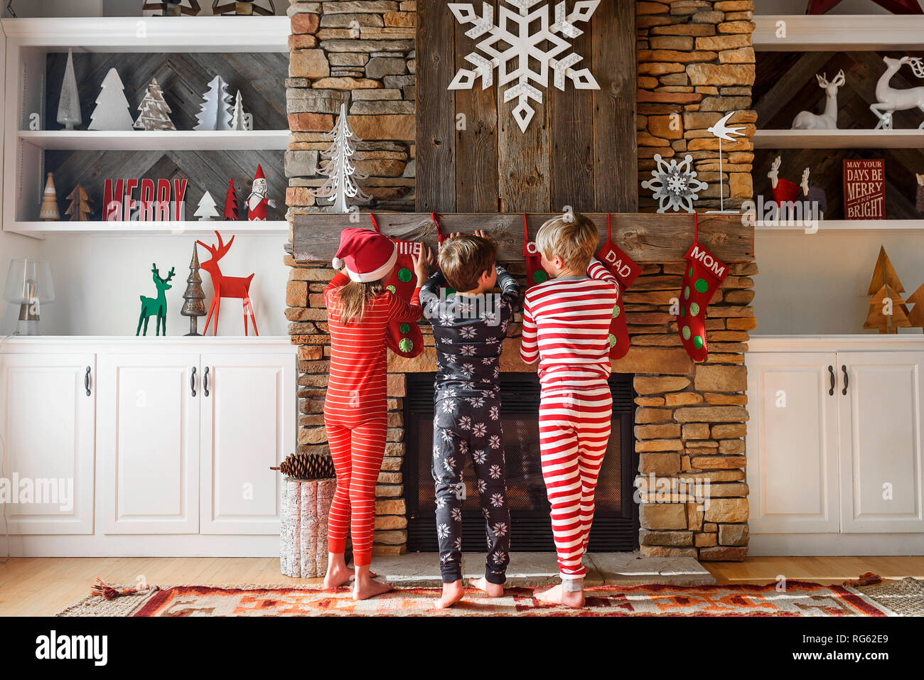Trois enfants d'accrocher des bas de Noël sur une cheminée Banque D'Images