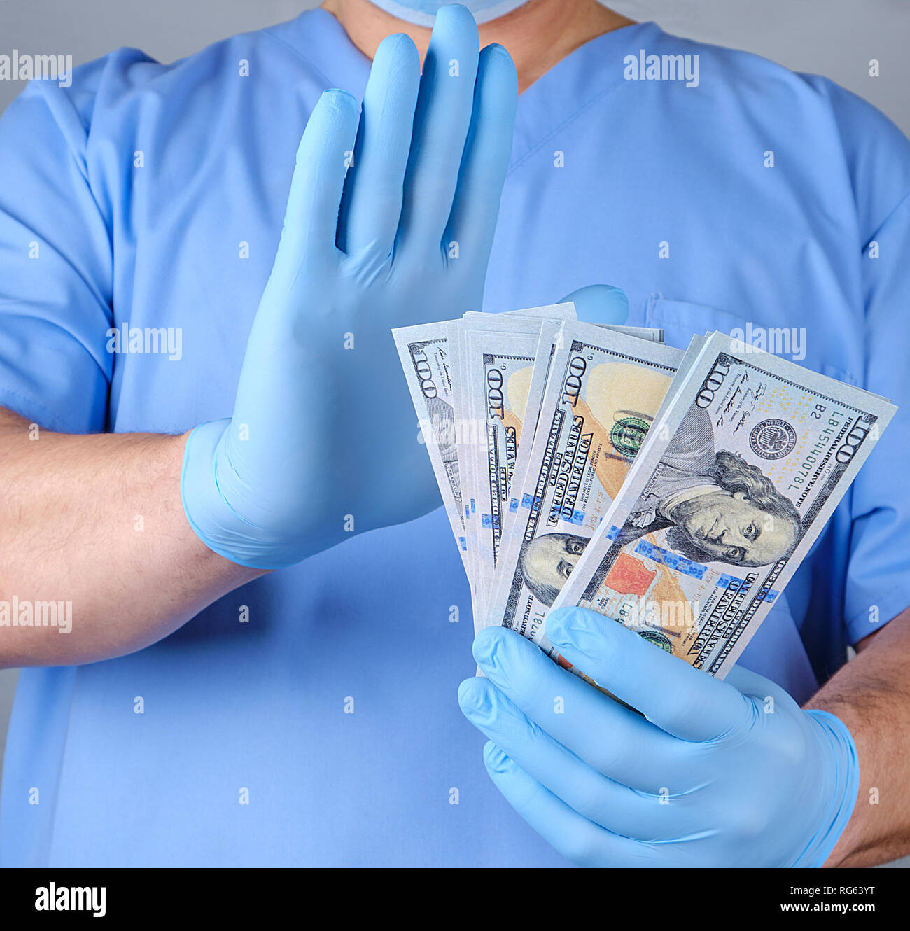 Médecin en uniforme bleu et des gants de datex est titulaire d'un lot de papier monnaie et avec un geste de main montre le refus de prendre de dollars Banque D'Images