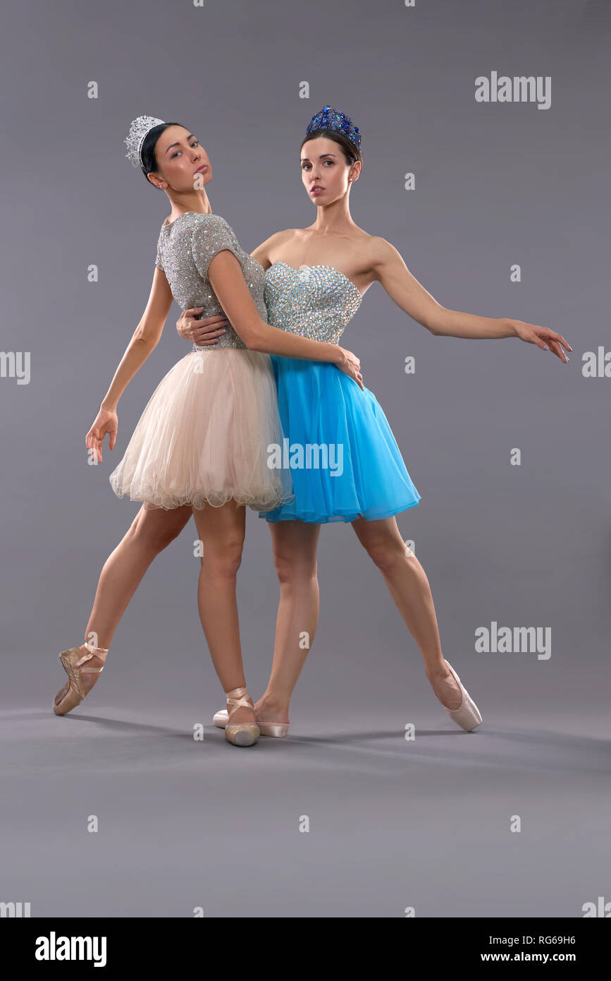 Deux jeunes ballerines debout sur les chaussettes, serrant les uns les  autres et à la recherche à l'appareil photo en studio. Danseurs de ballet  professionnel posant sur fond isolé gris. Concept de