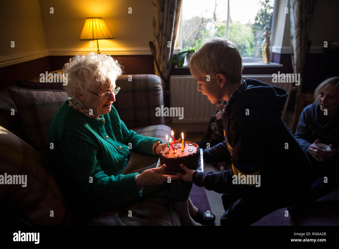 Femme âgée et petit-fils célébrant son anniversaire avec un gâteau tout en soufflant les bougies, Angleterre, Royaume-Uni Banque D'Images
