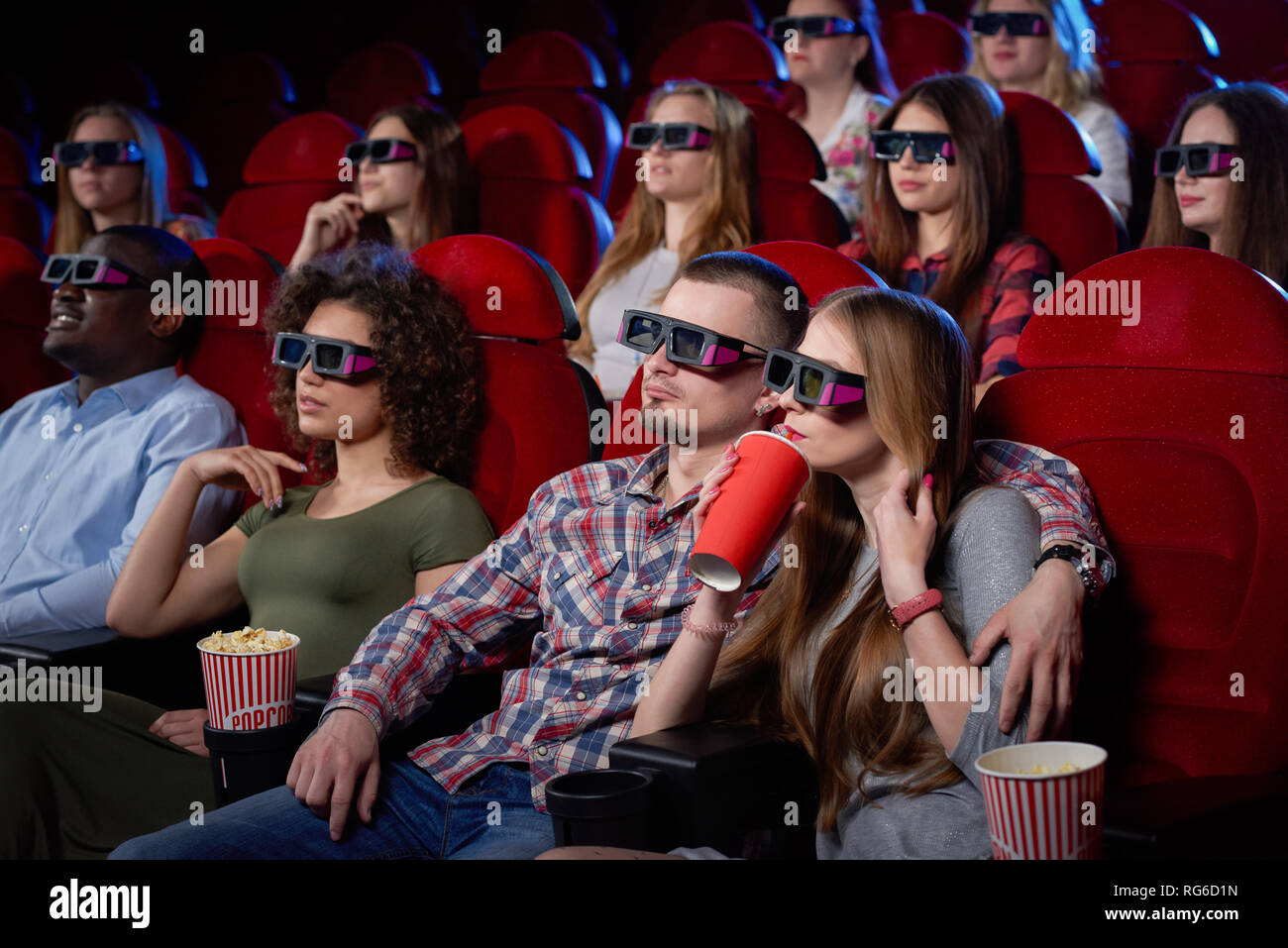 Vue latérale du joli couple ayant date et regarder la vidéo en 3D au cinéma. Jeune fille et un homme assis ensemble et enlacés, eating popcorn regarder la comédie. Notion de divertissement. Banque D'Images