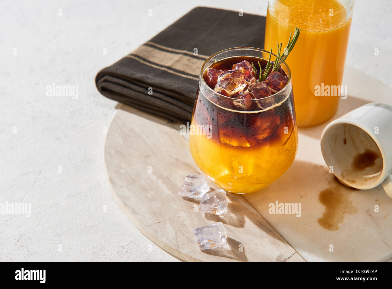 Froid de glace boisson d'été. Expresso jus d'orange avec de la glace, une bouteille de jus d'orange bio et vide d'espresso sur une assiette de marbre blanc sur fond blanc Banque D'Images