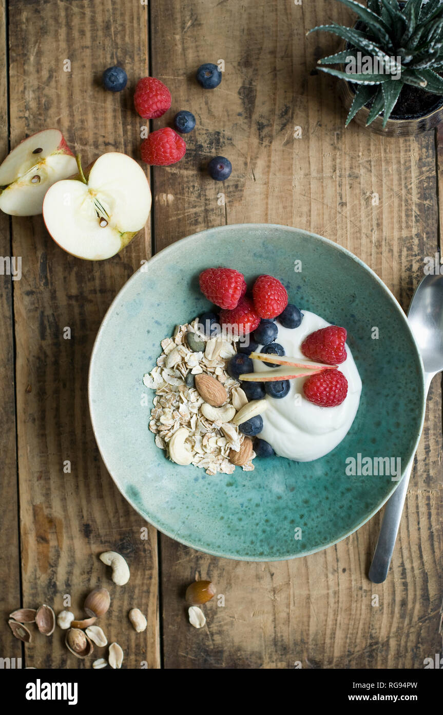 Bol de petit-déjeuner avec des céréales, yaourts, noix, pomme, framboise, myrtille sur bois Banque D'Images