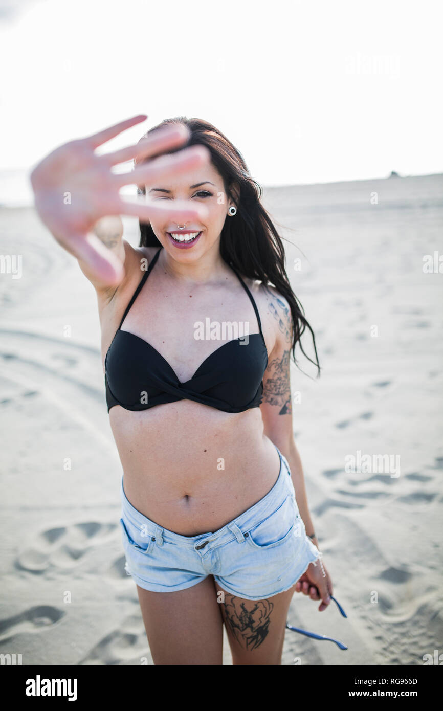 Portrait de jeune femme avec tatouage et piercing à la recherche à travers ses doigts sur la plage Banque D'Images