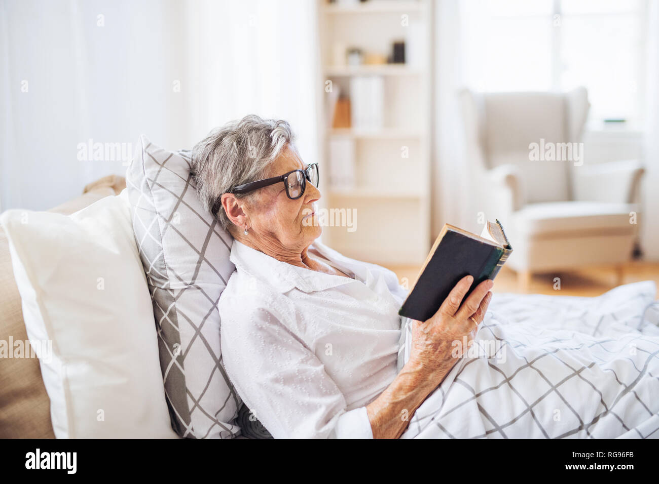 Une femme avec des lunettes senior malade au lit à la maison ou à l'hôpital, la lecture du livre de la bible. Banque D'Images