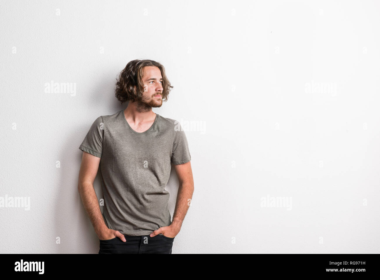 Portrait of a young man holding joyeuse à la longue chevelure ondulée dans un studio, les mains dans les poches. Copier l'espace. Banque D'Images